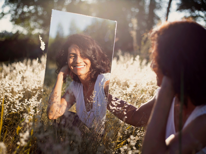 Woman looking in a mirror in a field